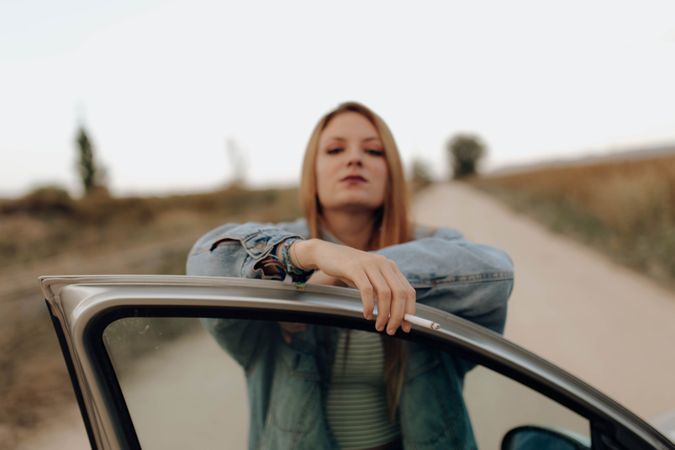 Modern woman with cigarette near car in nature
