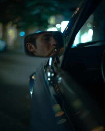 Young man's reflection while smoking on car rear mirror