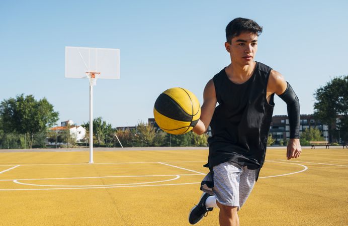 Young man playing on basketball court outdoor.