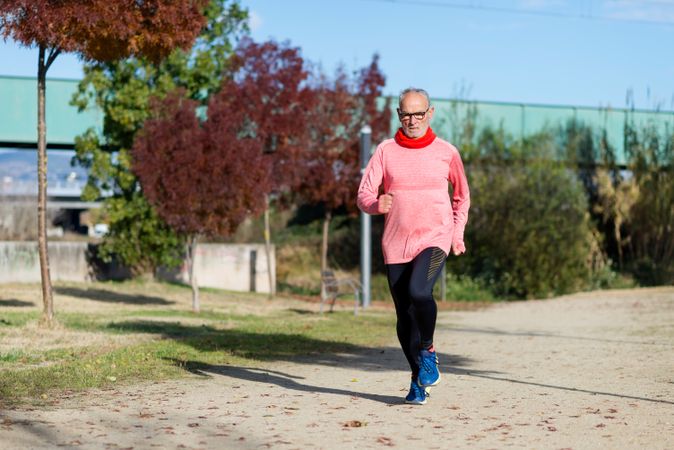 Mature man in red shirt jogging outside in park