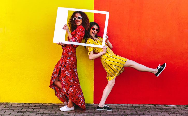 Silly female travelers posing at camera with empty picture frame