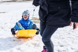 Excited son riding sledge near mother
