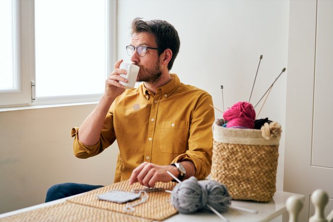 Man drinking hot tea during knitting