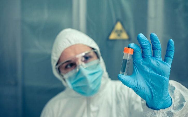 Scientist with protection suit looking vial in the laboratory