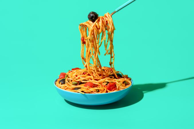 Eating spaghetti puttanesca from a bowl, minimalist on a green background