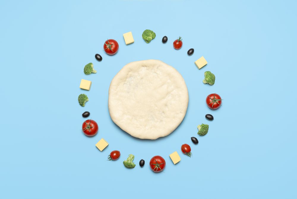 Raw pizza dough and vegetables on blue table