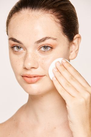 Peaceful female applying toner on radiant face with sponge