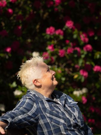 Side view of woman with spiky grey hair in front of flower bush