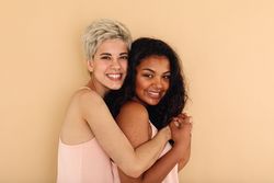 White blonde woman hugging biracial friend in studio shoot