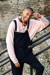 Happy male in overalls and hoodie leaning on railing of stairs outside, vertical