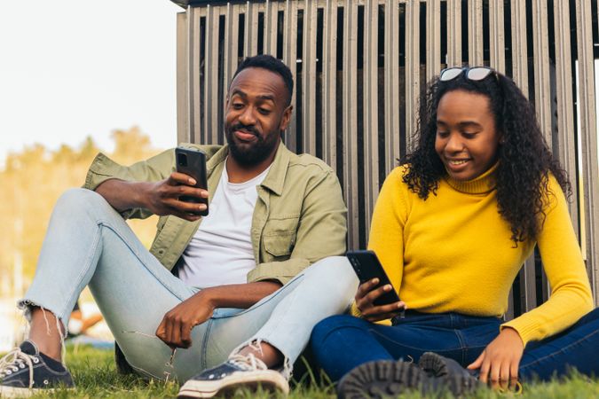Black couple sitting in a park using mobile