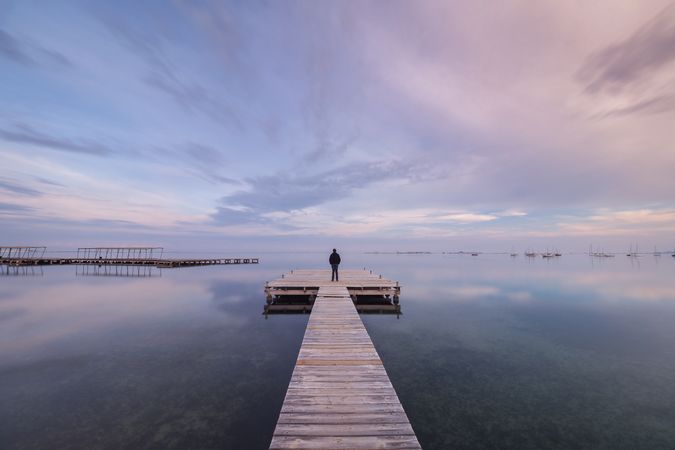 Anonymous person on wooden pier on cloudy evening