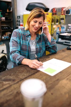 Portrait of smiling blonde young woman receiving order by phone for ecommerce shop