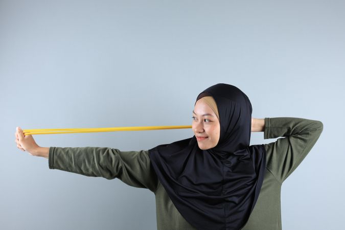 Young Asian Hijab Woman Stretch Yellow Resistance Band for Hand Pilates Exercise