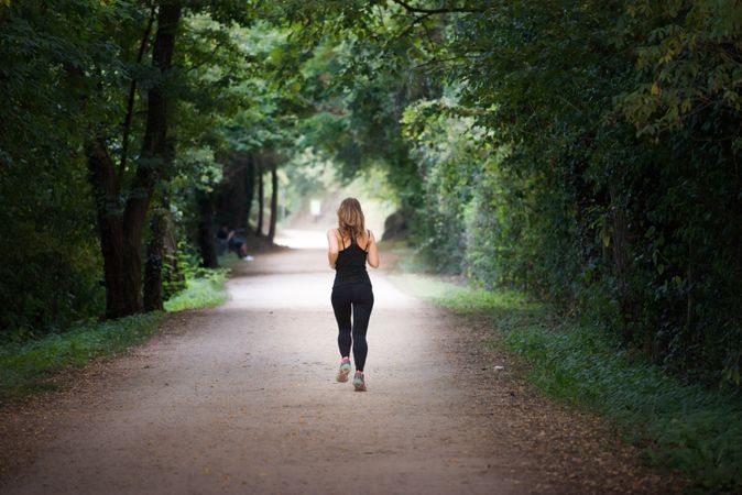 young fit woman running away doing sport on a path in park