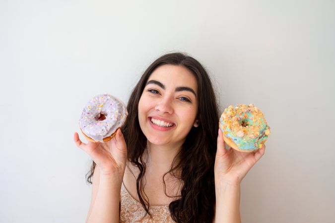 Playful woman making glasses of donuts while standing by white wall