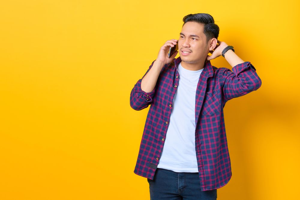 Asian male in argument on cell phone in yellow studio shoot