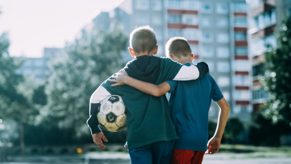 Two Young Boys Embracing Each Other while Walking in Neighborhood Football Pitch.