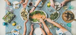 Group of people at blue patterned table serving themselves fish, and vegetable side dishes