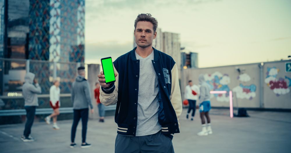 Young Stylish Man Standing in a City Environment, Diverse People Playing Street Soccer in the Background