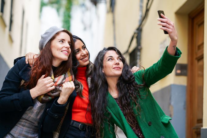 Three smiling female friends dressed in fall clothes taking selfie