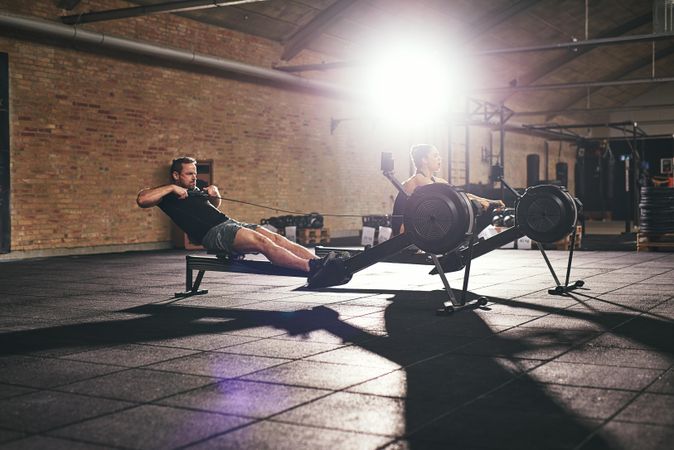 Two fit trainers using row machines in spacious modern gym