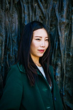 Pensive Asian woman leaning on rough wall