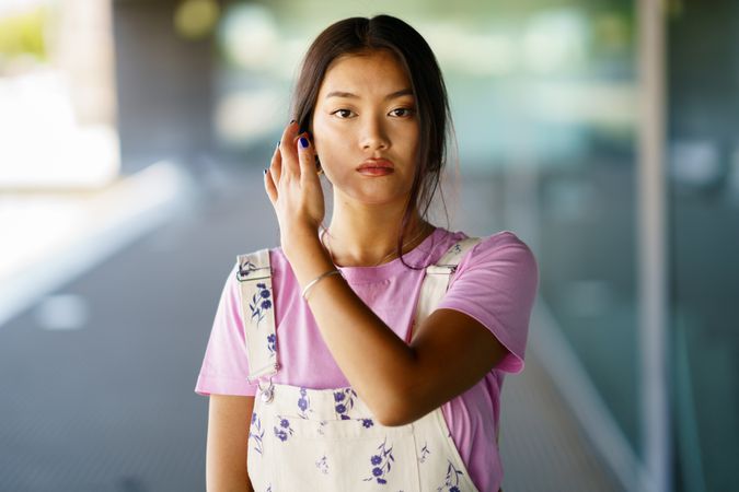 Chinese female in floral overalls and pink t-shirt adjusting her hair outside