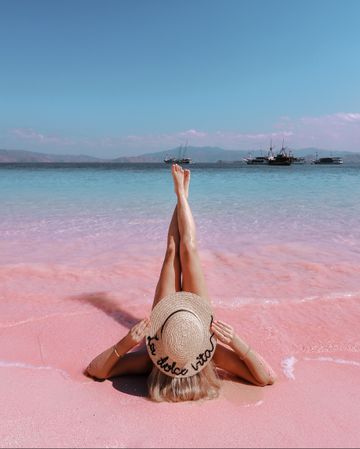 Woman in brown sun hat lying on pink beach in Indonesia