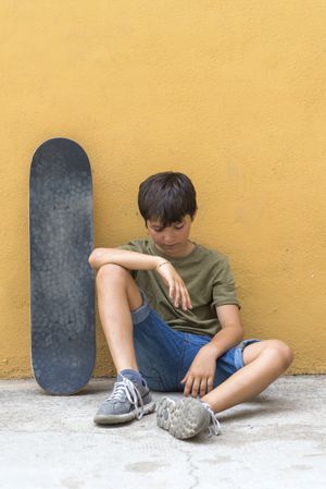 Front view of a young boy sitting on ground looking down