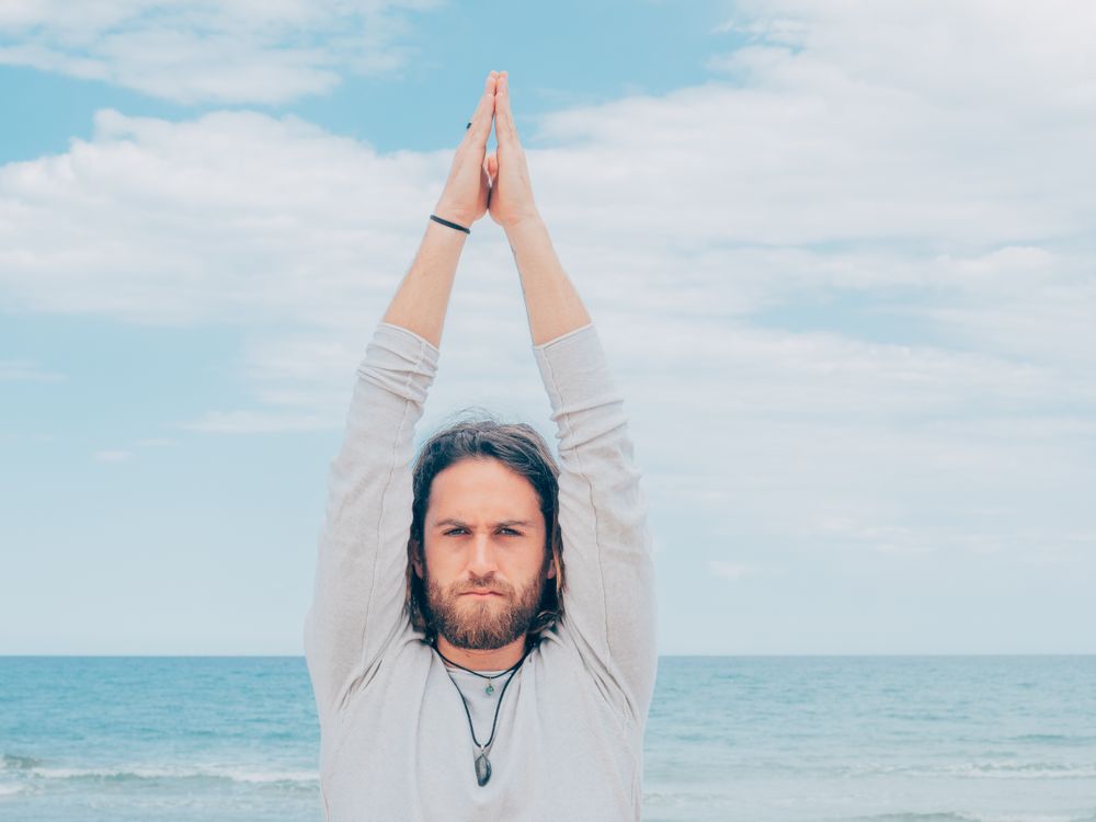 Man training yoga on beach