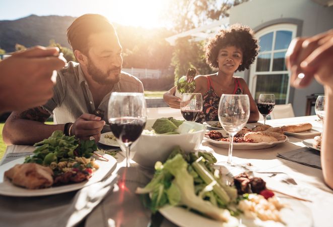 Woman pouring wine for man while enjoying dinner with friends