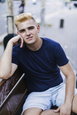Portrait of a young male with blonde hair sitting on a bench outside