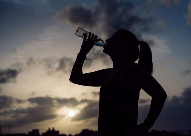 Woman drinking water and sky with clouds at sunset