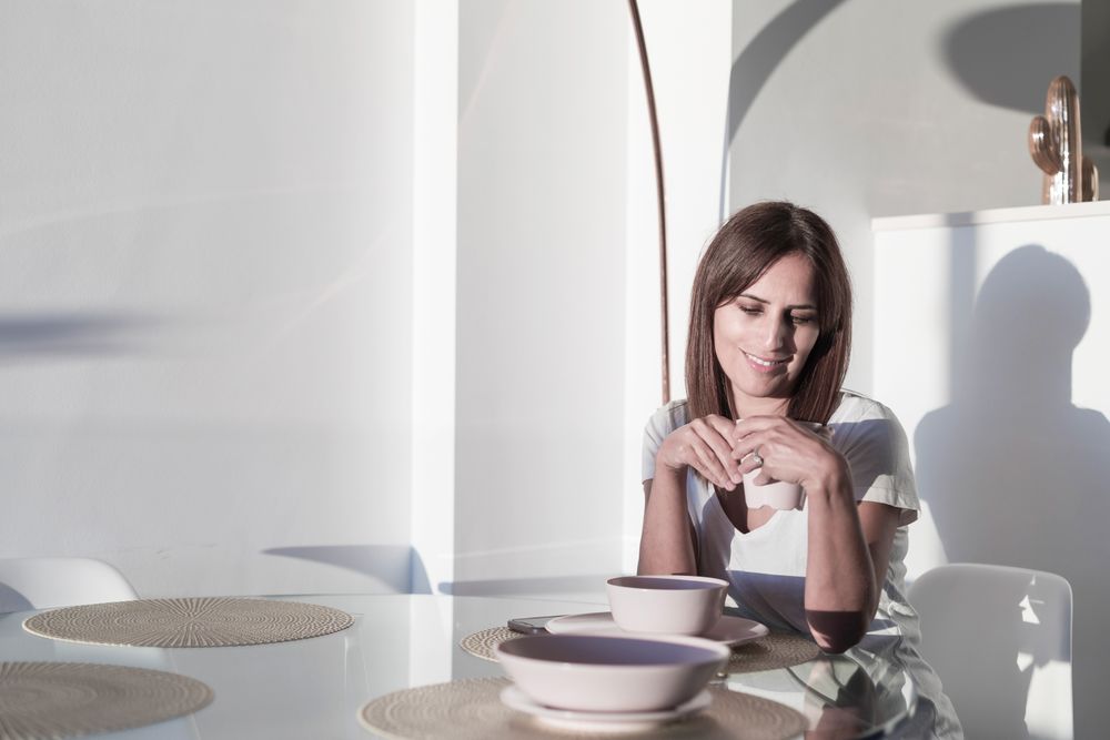 Smiling woman sitting at sunny table in front of bowl