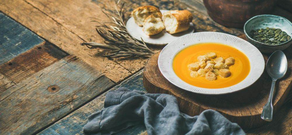 Pumpkin soup with croutons, seeds, spoon and bread on wooden table