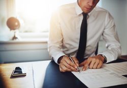 Man in shirt and tie writing with fountain pen in sunny office