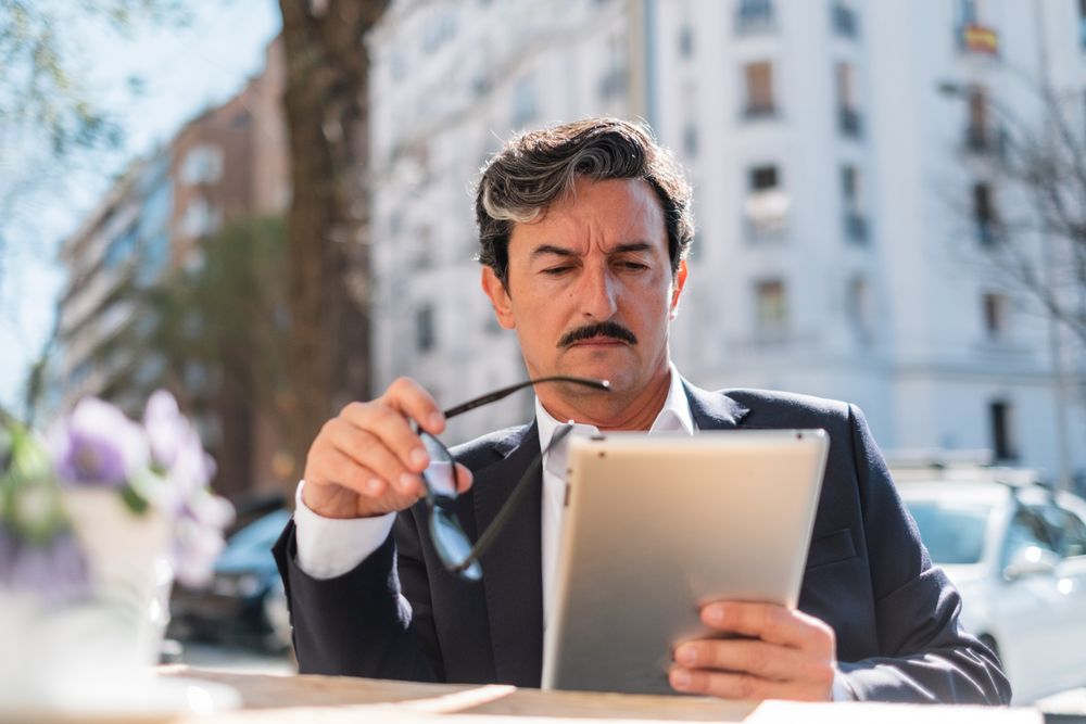 Wistful older man using gadget while relaxing at cafe