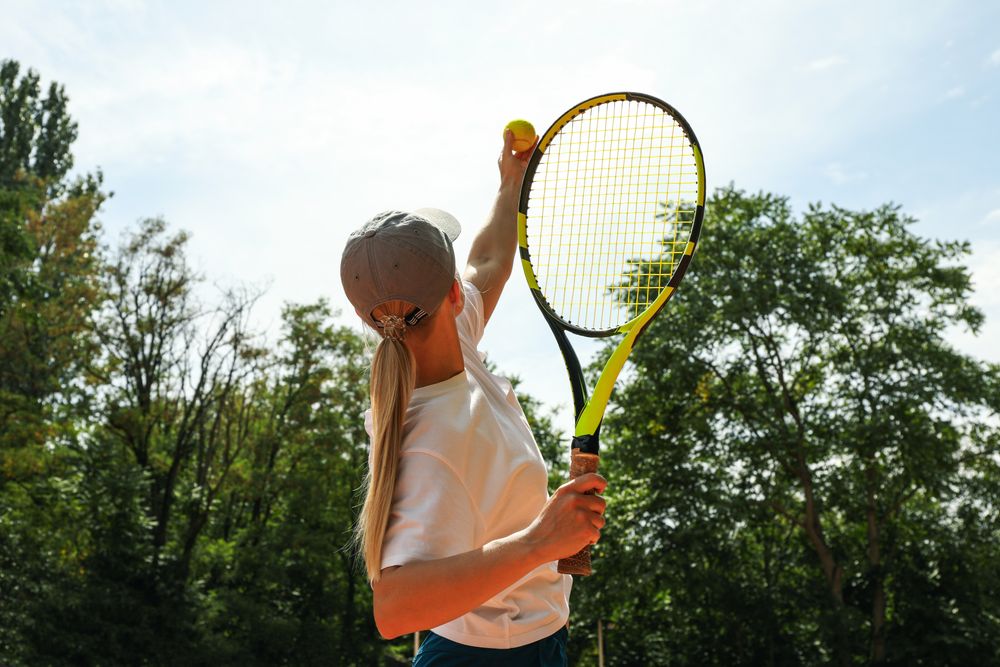 Young woman in white t-shirt serve the tennis ball