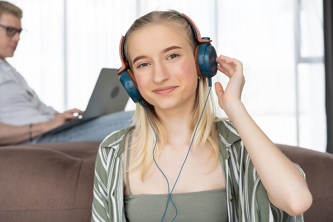 Portrait of happy young woman listening to music with headphone on sofa