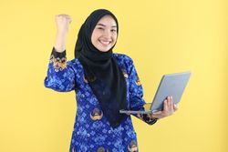 Indonesian Female or Civil Servant Excited While Holding Laptop, Wearing Korpri Blue Uniform.