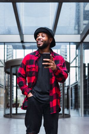 Cheerful Black male with smartphone in contemporary building