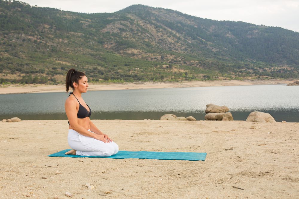 Woman practicing yoga outdoors near water
