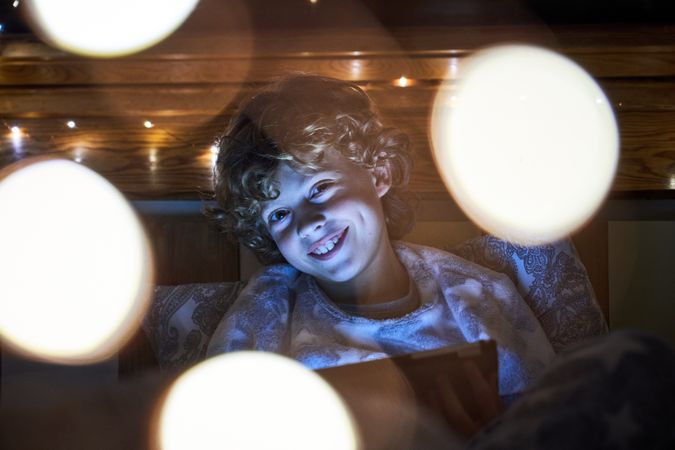 Cheerful boy browsing tablet in dark bedroom