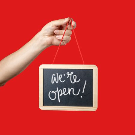 Hand holding a "We're open" sign on a red background.