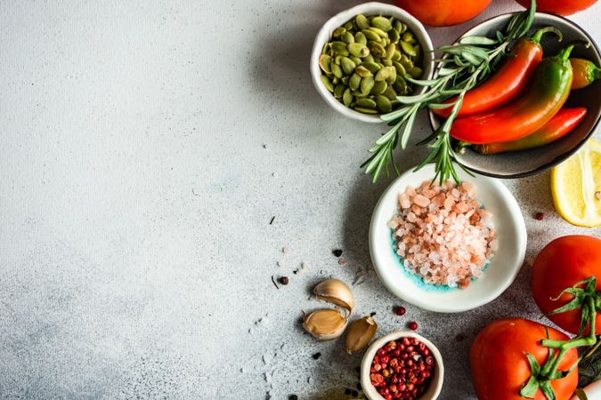 Top view of Himalayan salt, tomatoes, red peppercorns, pumpkin seeds, lemon, garlic & herbs on counter with copy space