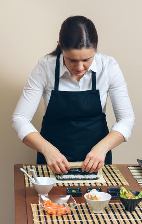 Female chef in apron rolling sushi in traditional mat