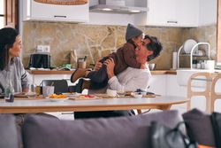 Happy father embracing anonymous daughter against wife in kitche