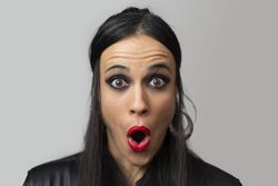 A young woman, with red lipstick and eye makeup, makes a surprised face with her mouth open