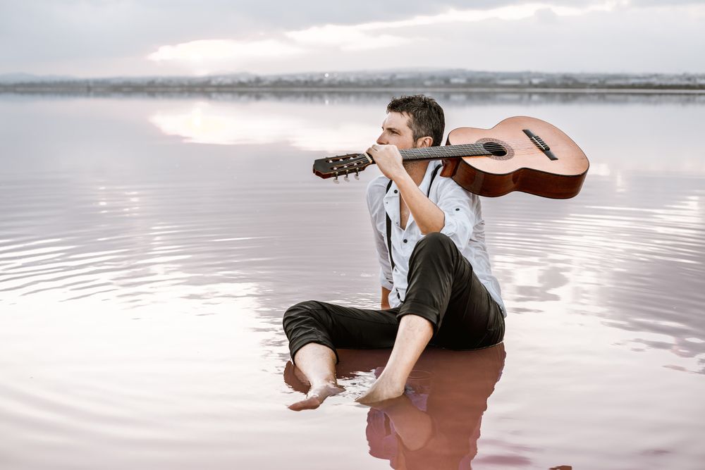 Musician with guitar on pink sandy water